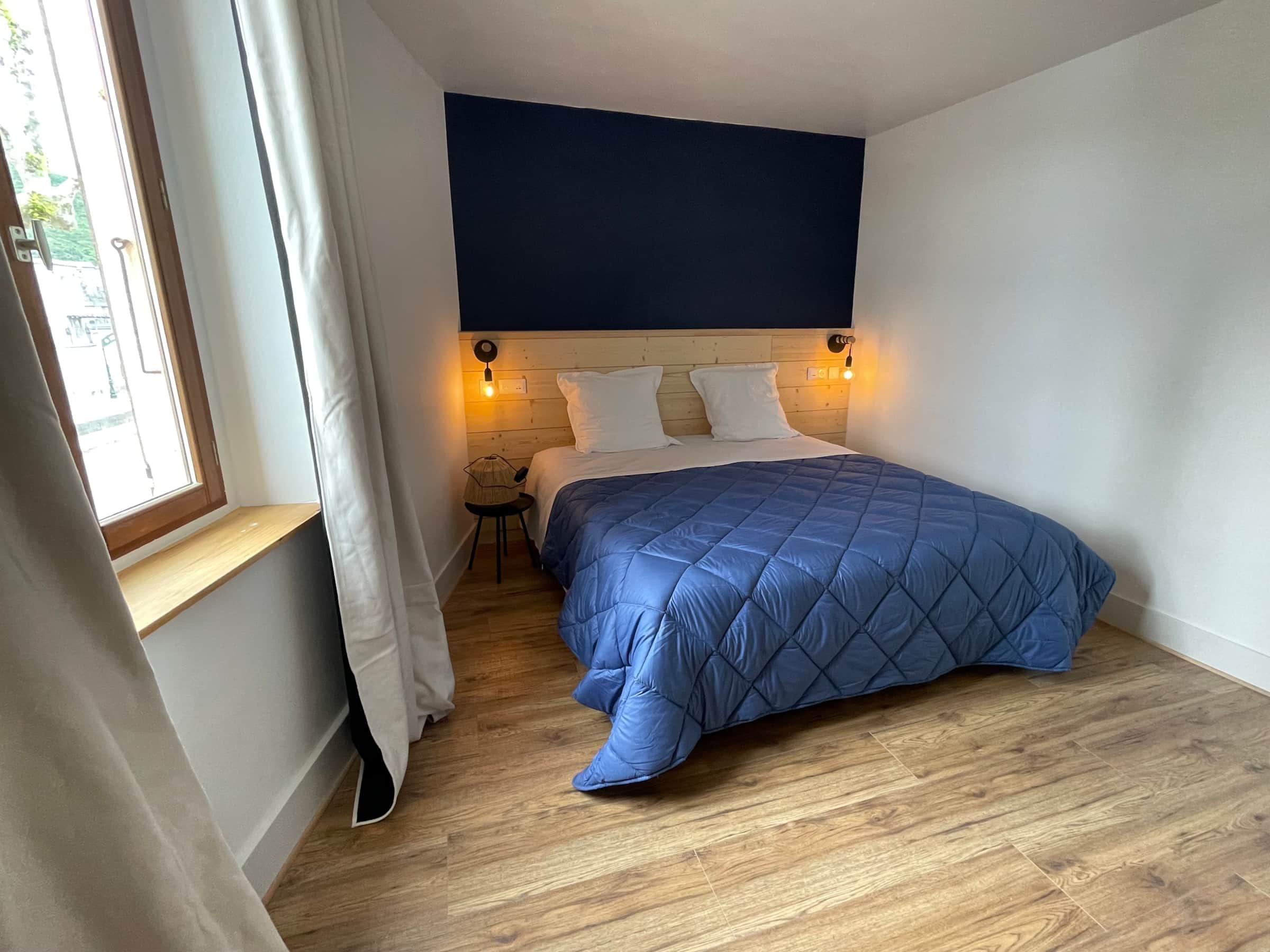 Chambre avec lit double, tête de lit en bois clair, appliques et rideaux en lin