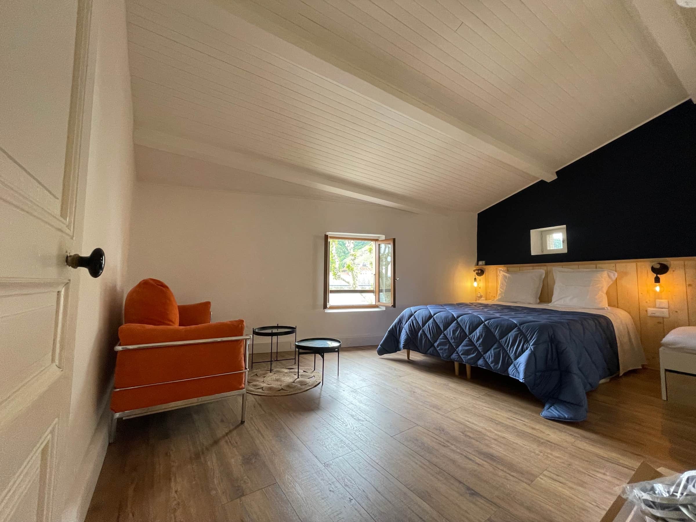 Chambre du second étage sous les combles, lit queen size, fauteuil orange et plafond lambrissé blanc