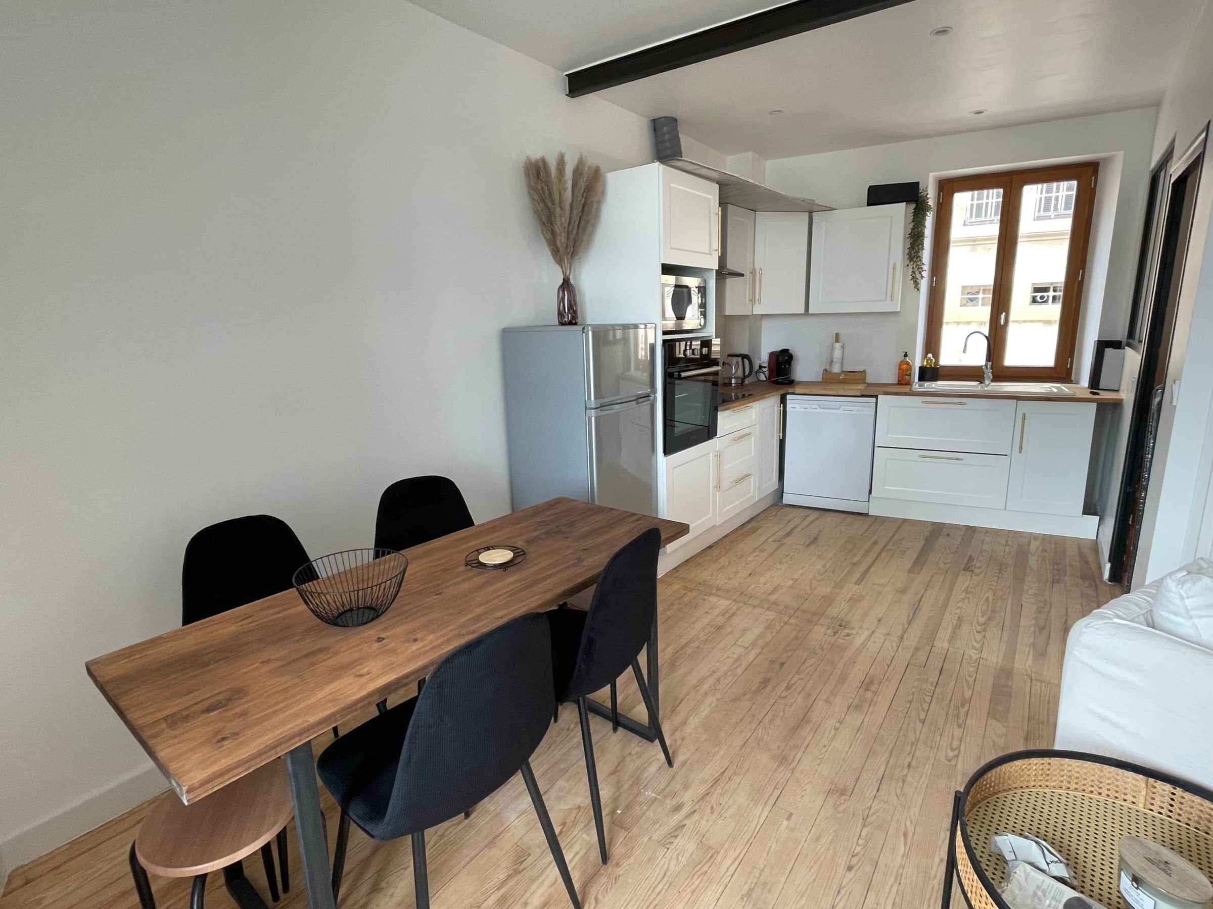 Cuisine équipée blanche avec four, micro-ondes, lave-vaisselle, machine à café et grande table en bois