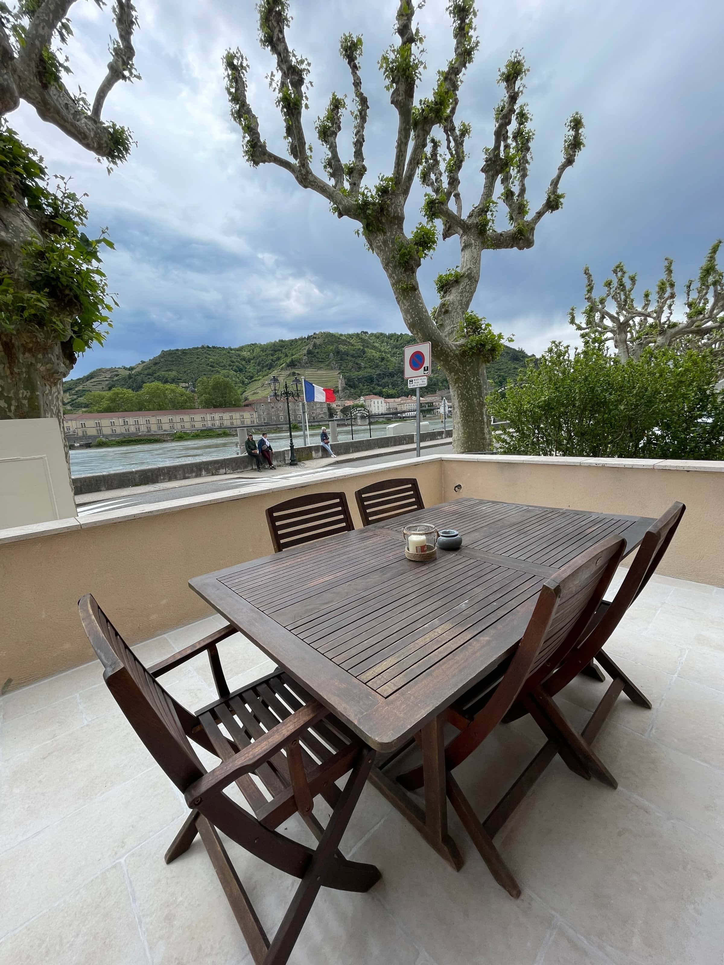 Terrasse de La Batellerie avec table en bois, vue directe sur le Rhône, les platanes et les coteaux de l'Hermitage